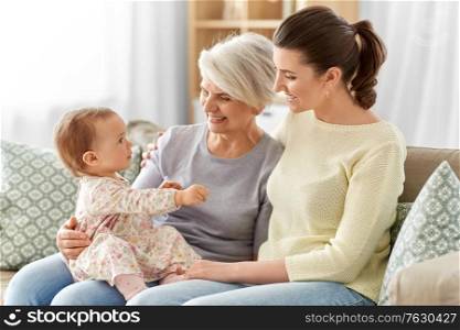 family, generation and female concept - happy smiling mother, baby daughter and grandmother sitting on sofa at home. mother, daughter and grandmother on sofa at home