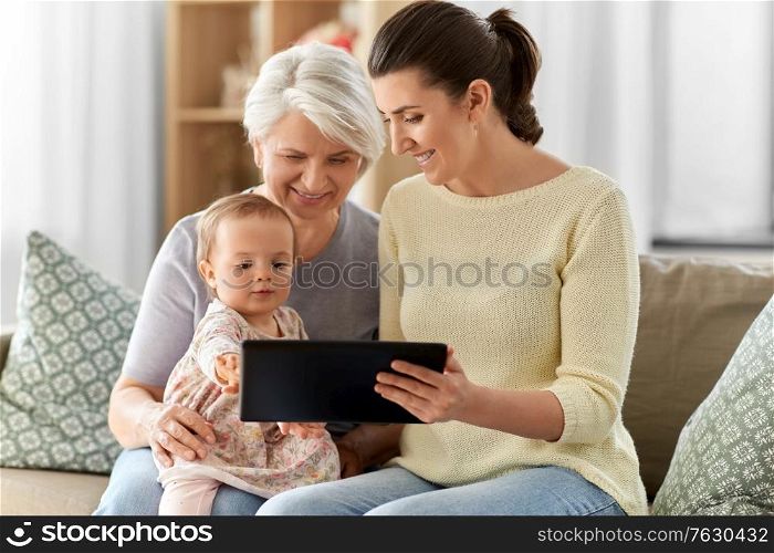 family, generation and female concept - happy smiling mother, daughter and grandmother sitting with tablet pc computer on sofa at home. mother, daughter and grandma with tablet pc