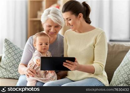 family, generation and female concept - happy smiling mother, daughter and grandmother sitting with tablet pc computer on sofa at home. mother, daughter and grandma with tablet pc