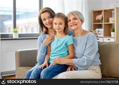 family, generation and female concept - portrait of smiling mother, daughter and grandmother sitting on sofa at home. portrait of mother, daughter and grandmother