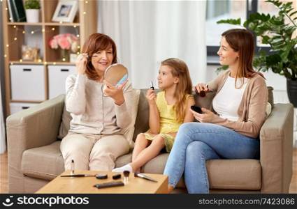 family, generation and female concept - portrait of smiling mother, daughter and grandmother with cosmetics doing make up at home. mother, daughter and grandmother doing make up