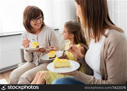 family, generation and food concept - smiling mother, daughter and grandmother eating cake at home. mother, daughter and grandmother eating cake