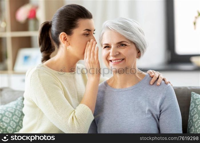 family, generation and people concept - adult daughter whispering secret to happy smiling senior mother at home. adult daughter whispering secret to senior mother