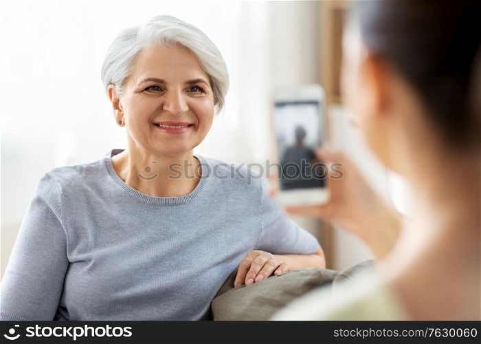 family, generation and people concept - adult daughter with smartphone photographing happy smiling senior mother at home. adult daughter photographing senior mother at home