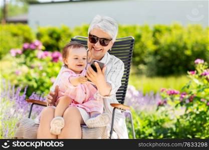 family, generation and people concept - happy grandmother and baby granddaughter with smartphone at summer garden. grandmother and baby granddaughter with phone