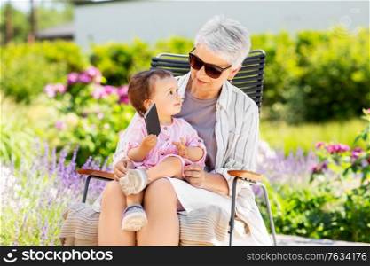 family, generation and people concept - happy grandmother and baby granddaughter with smartphone at summer garden. grandmother and baby granddaughter with phone