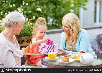 family, generation and people concept - happy grandmother and mother giving present to little daughter at cafe or restaurant terrace. happy mother giving present to daughter at cafe