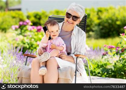 family, generation and people concept - happy grandmother with baby granddaughter calling on smartphone at summer garden. grandmother and baby granddaughter with smartphone