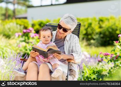 family, generation and people concept - happy grandmother with baby granddaughter reading book at summer garden. grandmother and baby granddaughter reading book