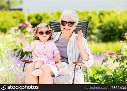 family, generation and people concept - happy grandmother with baby granddaughter waving hands at summer garden. happy grandmother and baby granddaughter at garden