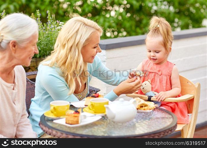 family, generation and people concept - happy mother, daughter and grandmother eating dessert at cafe or restaurant terrace. mother, daughter and grandmother eating at cafe