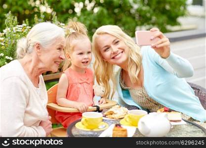 family, generation and people concept - happy mother, daughter and grandmother taking selfie by smartphone at cafe or restaurant terrace. happy family taking selfie at cafe