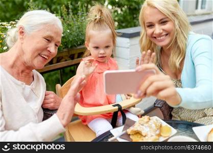 family, generation and people concept - happy mother, daughter and grandmother taking selfie by smartphone at cafe or restaurant terrace. happy family taking selfie at cafe
