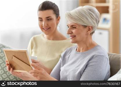 family, generation and people concept - happy smiling adult daughter and senior mother looking at photo at home. adult daughter and old mother with photo at home