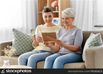 family, generation and people concept - happy smiling adult daughter and senior mother looking at photo at home. adult daughter and old mother with photo at home