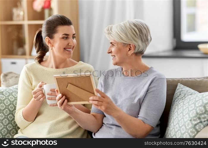 family, generation and people concept - happy smiling adult daughter and senior mother with at photo frame talking at home. adult daughter and old mother with photo at home