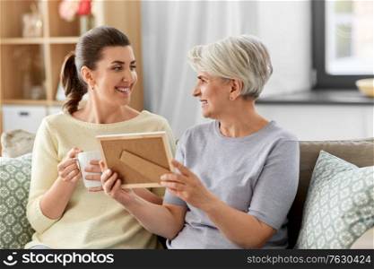family, generation and people concept - happy smiling adult daughter and senior mother with at photo frame talking at home. adult daughter and old mother with photo at home