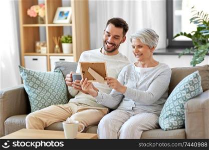 family, generation and people concept - happy smiling adult son and senior mother looking at photo at home. adult son and senior mother with photo at home