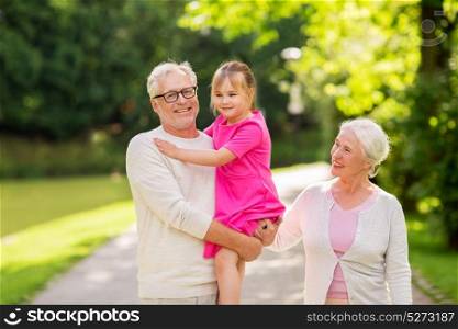 family, generation and people concept - happy smiling grandmother, grandfather and little granddaughter at park. senior grandparents and granddaughter at park