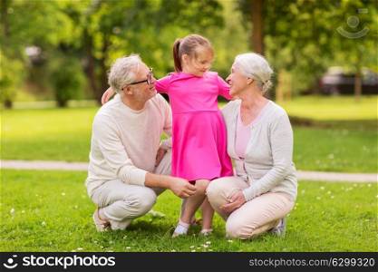 family, generation and people concept - happy smiling grandmother, grandfather and little granddaughter at park. senior grandparents and granddaughter at park