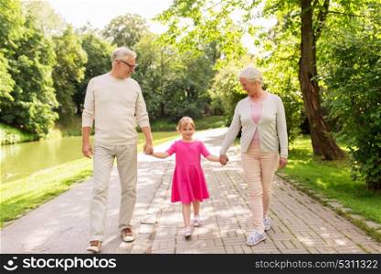 family, generation and people concept - happy smiling grandmother, grandfather and little granddaughter walking at park. senior grandparents and granddaughter at park