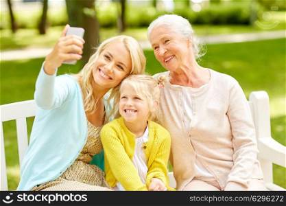 family, generation and people concept - happy smiling mother with daughter and grandmother taking selfie by smartphone at park. mother with daughter and grandmother at park