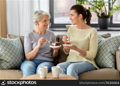 family, generation and people concept - happy smiling senior mother and adult daughter eating cake at home. old mother and adult daughter eating cake at home