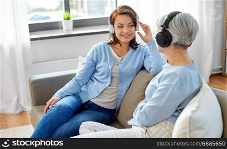 family, generation and people concept - happy smiling senior mother in headphones talking to adult daughter at home. senior mother and adult daughter with headphones