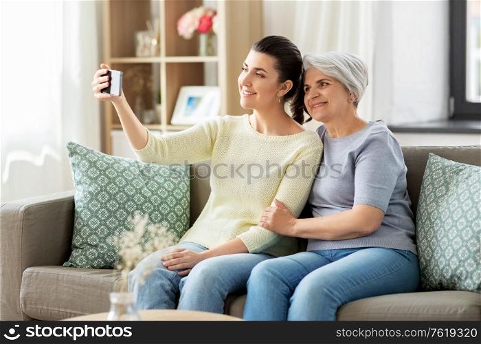 family, generation and people concept - happy smiling senior mother with adult daughter taking selfie by smartphone at home. senior mother with daughter taking selfie at home