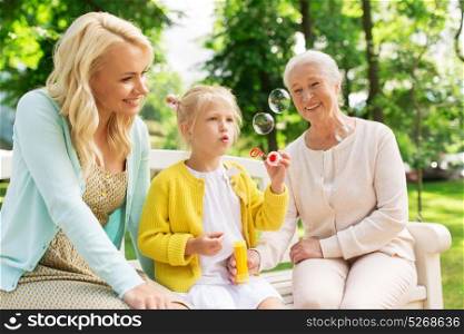 family, generation and people concept - happy smiling woman with senior mother and little daughter blowing soap bubbles at park. happy family blowing soap bubbles at park