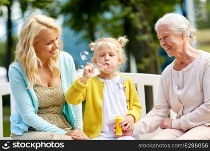 family, generation and people concept - happy smiling woman with senior mother and little daughter blowing soap bubbles at park. happy family blowing soap bubbles at park
