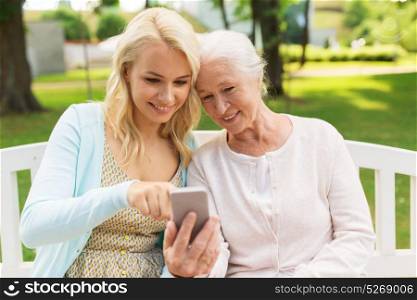 family, generation and people concept - happy smiling young daughter and senior mother with smartphone sitting on park bench. daughter and senior mother with smartphone at park