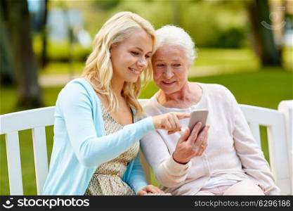 family, generation and people concept - happy smiling young daughter and senior mother with smartphone sitting on park bench. daughter and senior mother with smartphone at park
