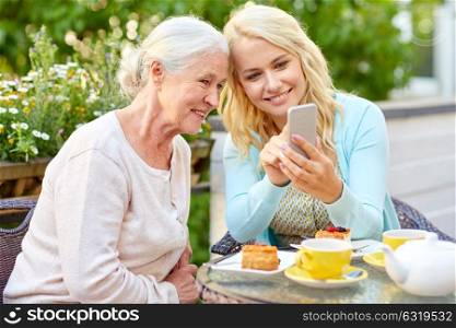 family, generation and people concept - happy smiling young daughter and senior mother with smartphone at cafe or restaurant terrace. daughter and senior mother with smartphone at cafe