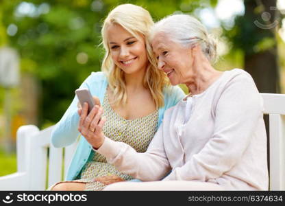 family, generation and people concept - happy smiling young daughter and senior mother with smartphone sitting on park bench. daughter and senior mother with smartphone at park