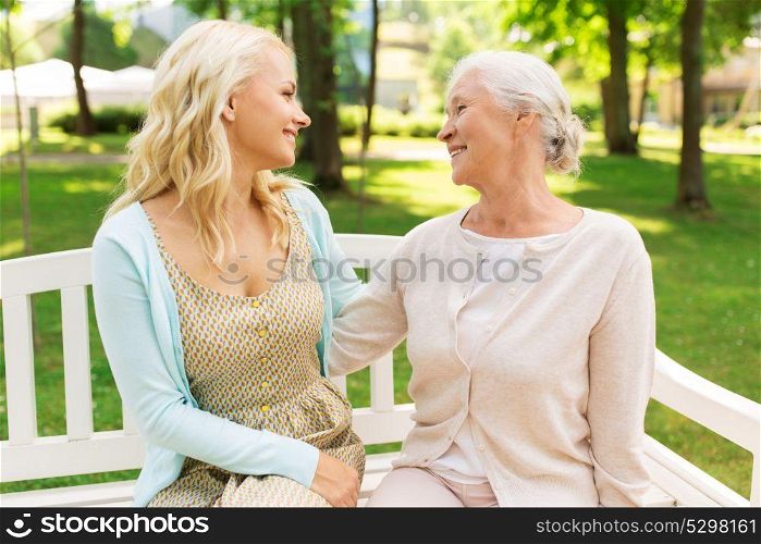 family, generation and people concept - happy smiling young daughter with senior mother sitting on park bench and hugging. daughter with senior mother hugging on park bench