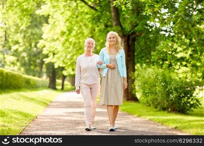 family, generation and people concept - happy smiling young daughter with senior mother walking at summer park. daughter with senior mother walking at summer park