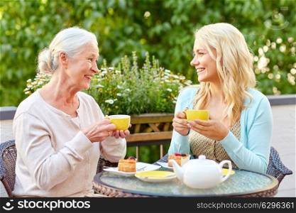 family, generation and people concept - happy smiling young daughter with senior mother drinking tea at cafe or restaurant terrace. daughter with senior mother drinking tea at cafe