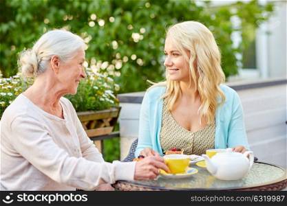 family, generation and people concept - happy smiling young daughter with senior mother drinking tea at cafe or restaurant terrace. daughter with senior mother drinking tea at cafe