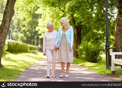 family, generation and people concept - happy smiling young daughter with senior mother walking at summer park. daughter with senior mother walking at summer park
