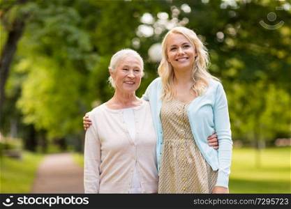 family, generation and people concept - happy smiling young daughter with senior mother hugging at summer park. daughter with senior mother hugging at park