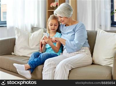 family, generation and technology concept - grandmother and granddaughter with smartphone at home. grandmother and granddaughter with smartphone