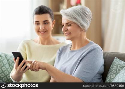 family, generation and technology concept - happy smiling senior mother and adult daughter with smartphone at home. daughter and senior mother with smartphone at home