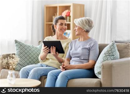 family, generation and technology concept - happy smiling senior mother and adult daughter with tablet pc computer at home. daughter and senior mother with tablet pc at home