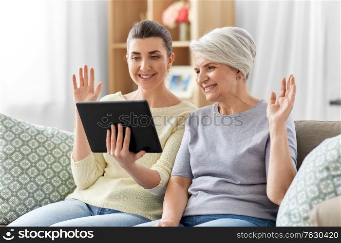 family, generation and technology concept - happy smiling senior mother and adult daughter with tablet pc computer having video call at home. daughter and mother having video call on tablet pc