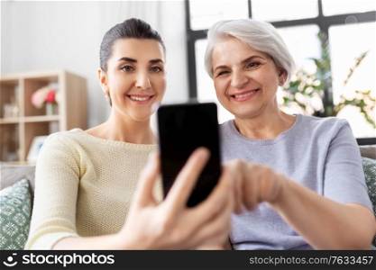 family, generation and technology concept - happy smiling senior mother and adult daughter with smartphone at home. daughter and senior mother with smartphone at home