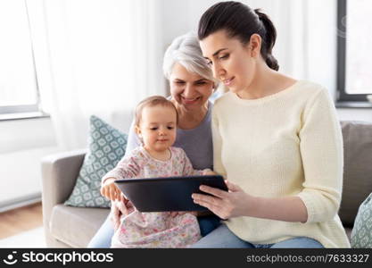 family, generation and technology concept - mother, daughter and grandmother sitting with tablet pc computer on sofa at home. mother, daughter and grandma with tablet pc