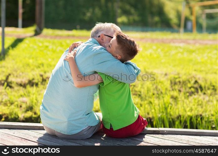 family, generation, communication and people concept - happy grandfather and grandson hugging on berth