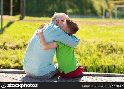 family, generation, communication and people concept - happy grandfather and grandson hugging on berth