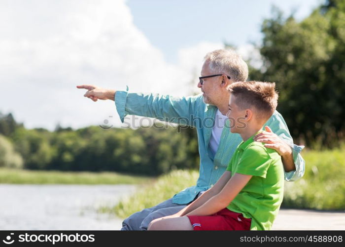 family, generation, communication and people concept - happy grandfather and grandson sitting on river berth